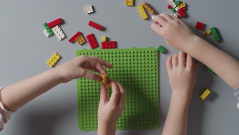 disparo aéreo de dos niños jugando con ladrillos de construcción de plástico sobre un fondo gris