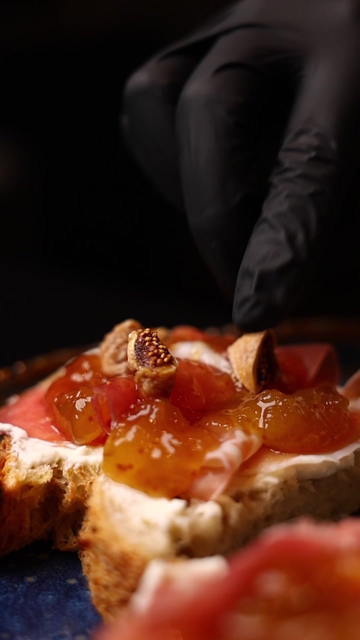 Chef che posiziona un fico su toast gourmet con prosciutto crudo e formaggio cremoso