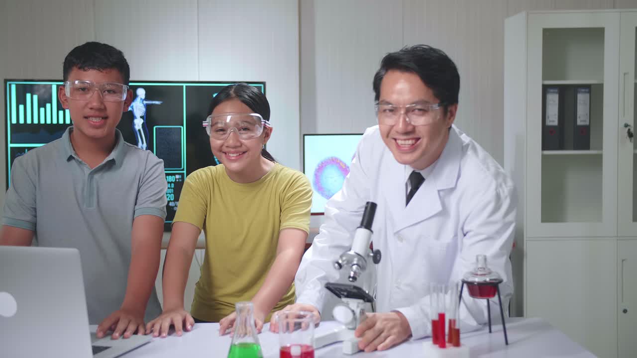 Young Asian Boy And Girl Learning Science Experiment In Laboratory With Teacher In Classroom, They Smile To Camera