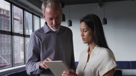 Diverse-business-colleagues-standing-using-digital-tablet-and-talking-in-office