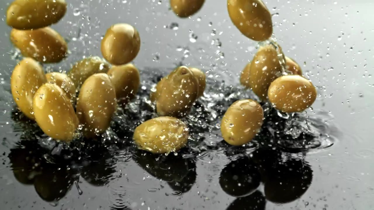 Olive verdi fresche che cadono e schizzano nell'acqua su una superficie scura.