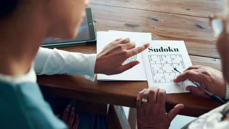 elderly woman doing sudoku puzzle with caregiver