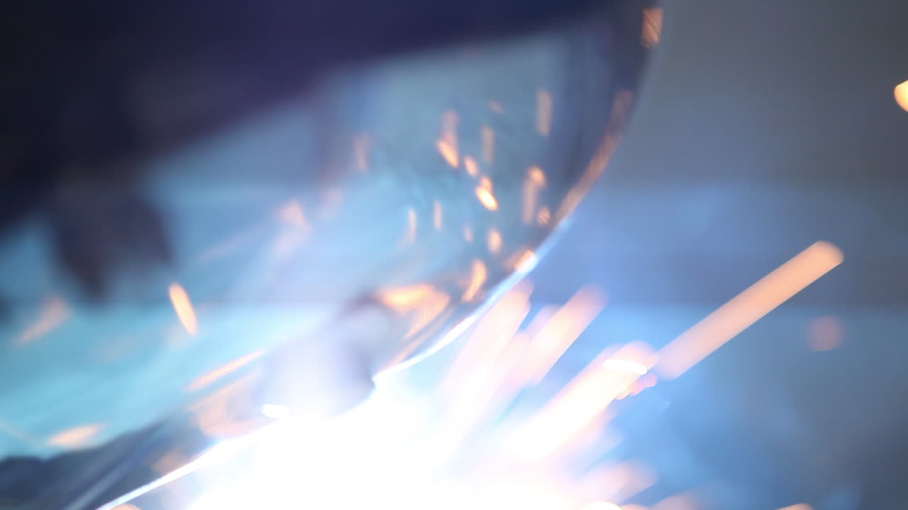 Scintille di saldatura che volano riflettendosi sulla visiera, creando un'immagine suggestiva.