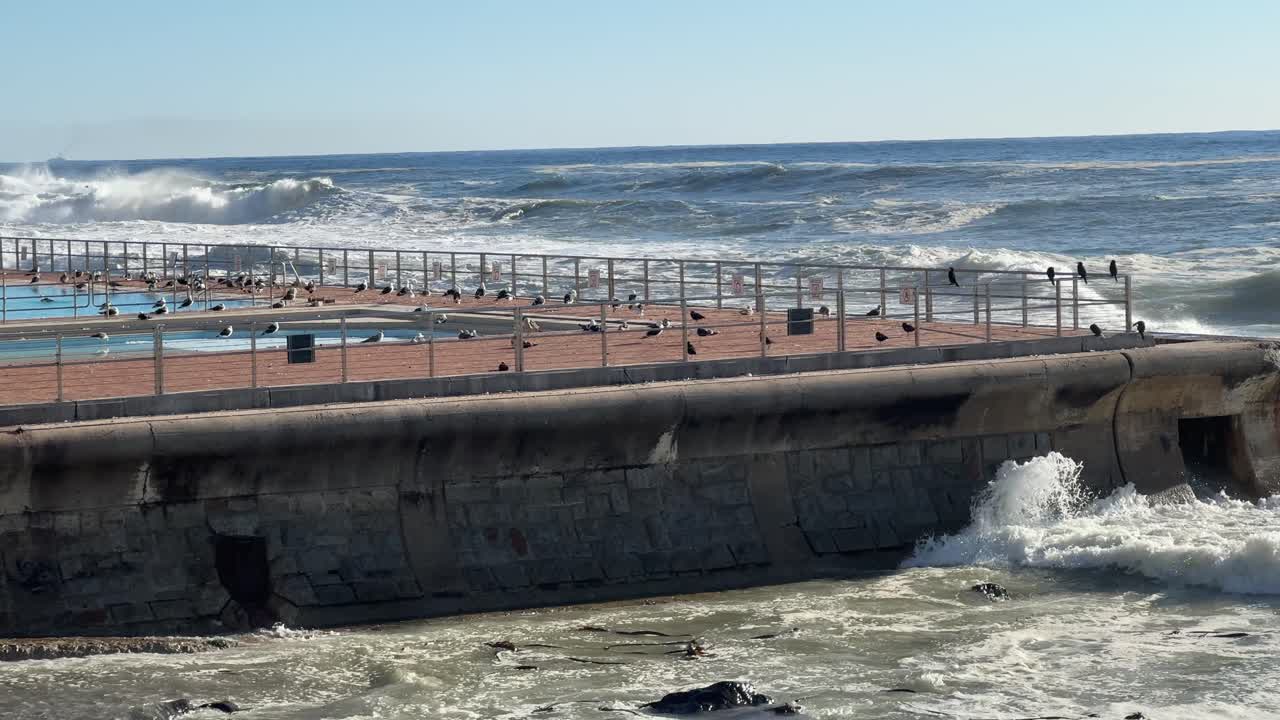 Waves crashing against the Sea Point Pool Wall on a sunny winter’s day in Sea Point, Cape Town, South Africa