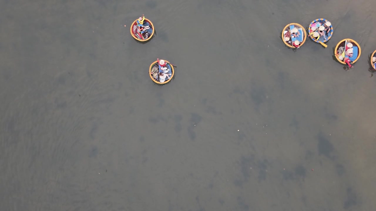 Perahu berbentuk kelapa yang mengangkut orang mengapung perlahan di air dangkal yang jernih di Hoi An, Vietnam, diambil dari perspektif drone tinggi