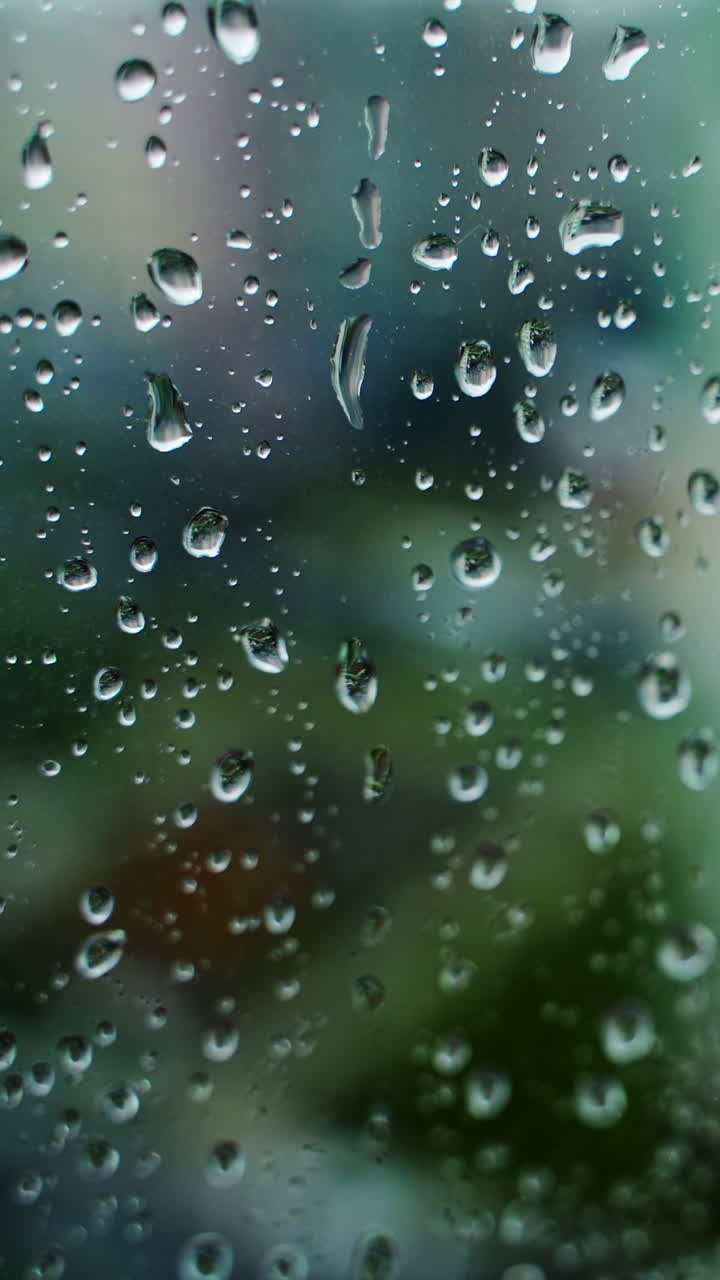 Rain drop on glass window on blur city view background. Raining weather. Water drops background. Close-up. Vertical video
