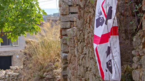 Pabellón-De-Cerdeña-Al-Lado-De-Un-Muro-De-Piedra-En-Un-Pequeño-Pueblo,-Vista-De-Mano