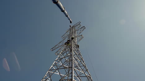 Looking-Up-Steel-Pylon-Tower-Against-Blue-Sky-With-Professional-Men-Working