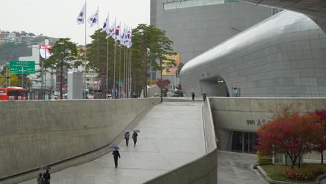 people walking with parasols in dongdaemoon design plaza on a rainy day in seoul, south korea. - wide shot
