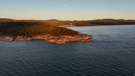 granite rocks along coast of bay of fires at dusk with full moon in the sky, tasmania in australia