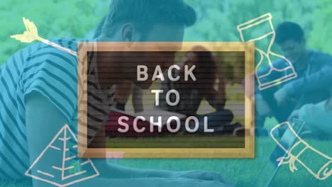 vuelta al texto de la escuela en pizarra de madera contra el estudiante masculino caucásico usando una computadora portátil en la hierba