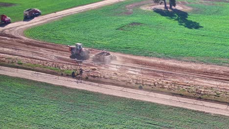 Tractor-and-small-road-grader-rounding-a-bend-in-dirt-road-and-passing-farm-vehicles