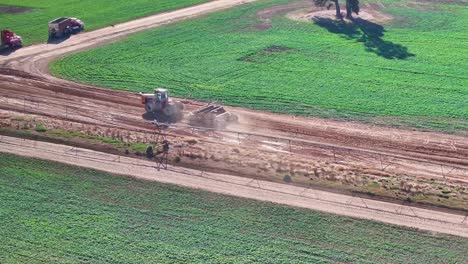tractor y pequeño nivelador de carretera redondeando una curva en una carretera de tierra y pasando vehículos agrícolas