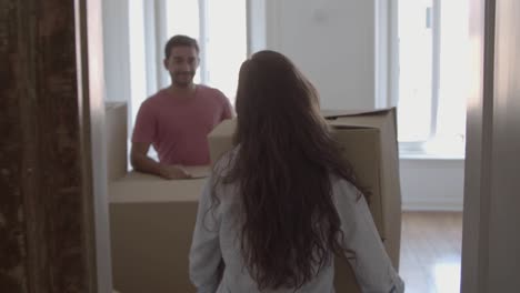 mujer feliz entrando a la habitación, cargando una caja con cosas diferentes y besando a su esposo