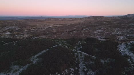 Glencoe-at-dusk-with-shadows-over-the-vast,-undulating-terrain-and-dense-forests,-aerial-view