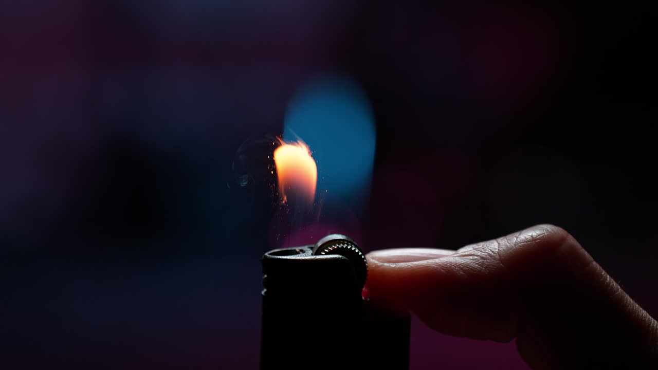golpeando un encendedor con un pulgar en macro y cámara lenta, las chispas encienden el gas generando una llama bailando sobre un fondo púrpura