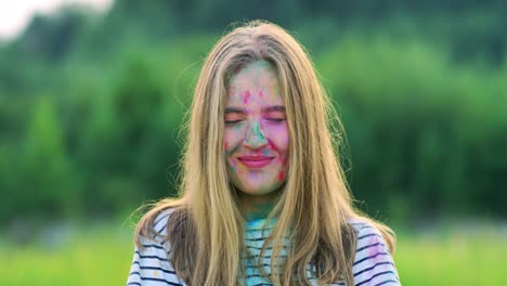 retrato de la joven alegre sonriendo mientras está de pie al aire libre en polvo de pintura en el festival holi