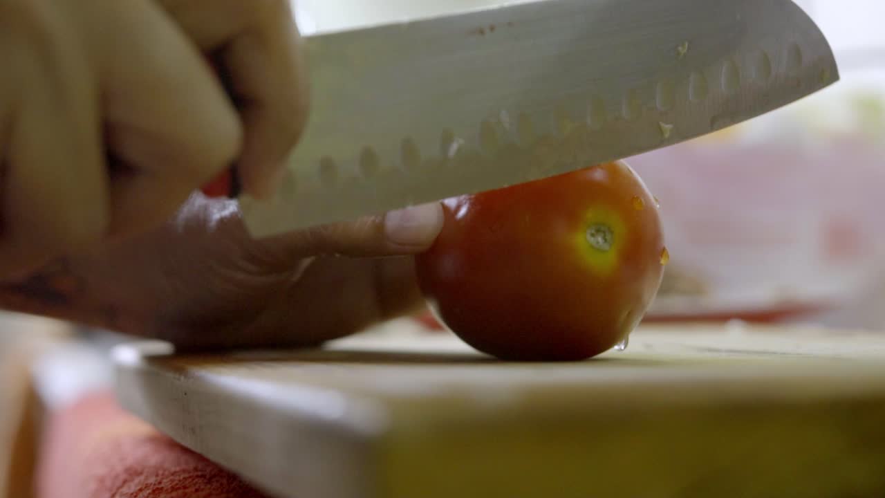 Primo piano dell'affettatura di pomodoro al rallentatore su tagliere con coltello affilato in cucina, alimenti freschi e cucina sana.