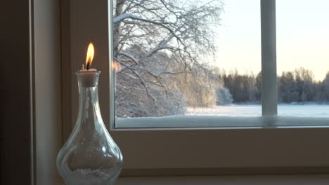 candlelight in bottle next to home window with snowy landscape outside