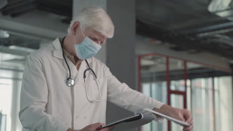 a grey haired, middle aged doctor in a facemask takes notes in a notebook 1