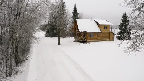 una tranquila y cálida cabaña de troncos de invierno durante una suave nevada con leña sentada en el porche delantero