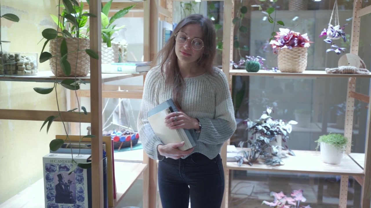 Jovem estudante entra, pega livros emprestados da estante da biblioteca e sai. Fundo orgânico escandinavo verde.