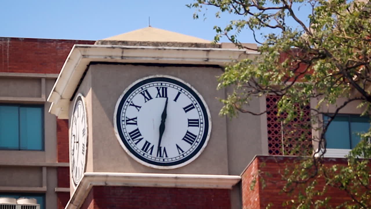 Primer plano de una torre de reloj en un edificio urbano con números romanos a la luz del día. Útil para contenido sobre plazos, horarios, puntualidad, gestión del tiempo y arquitectura urbana.