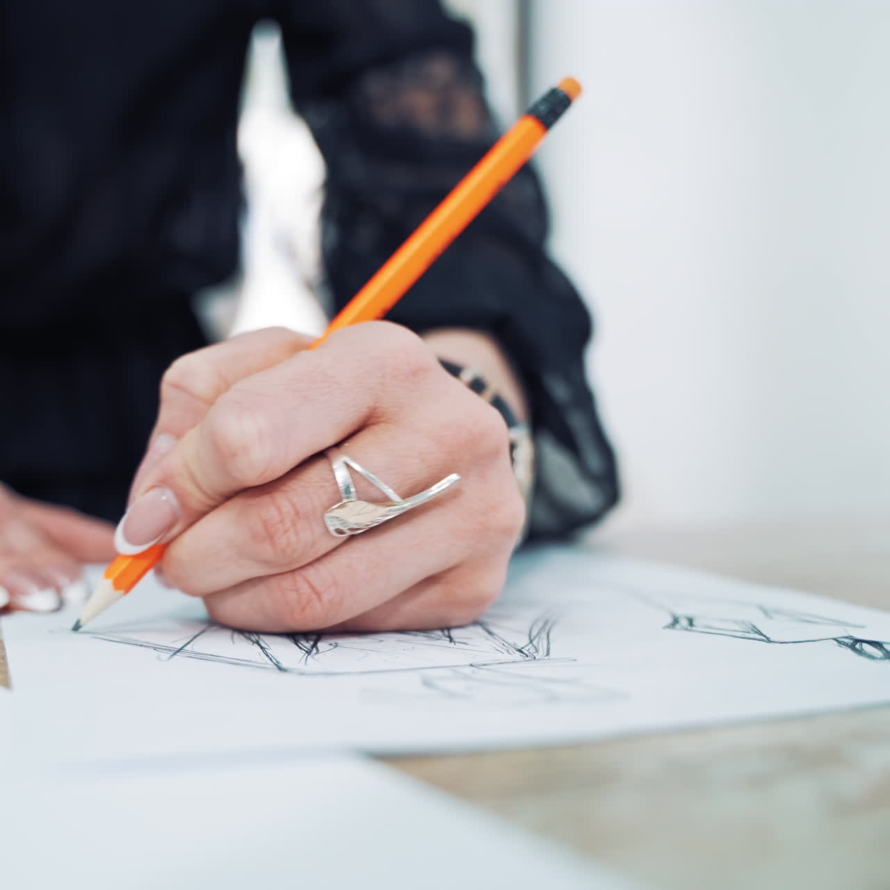 Hands of a fashion designer with a beautiful manicure draw a sketch with a pencil. Professional dressmaker creates a stylish design of a new dress on a sheet of paper. Close-up