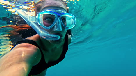 caucasian woman snorkeling and filming herself in the clear light blue waters of turtle paradise, indonesia.