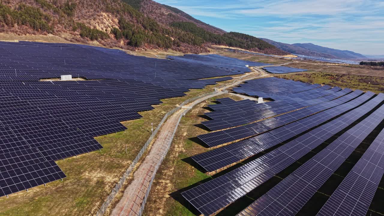 Solpaneler dækker landet i en dal nær bjerge på en klar dag