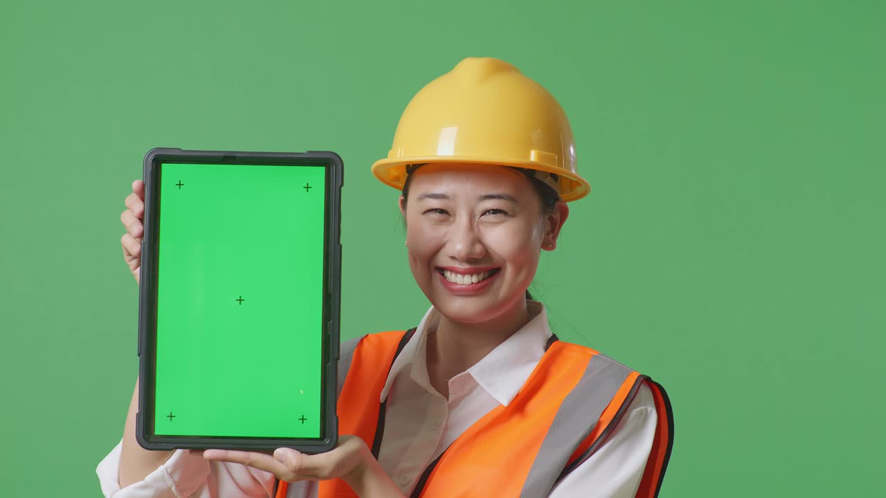 Close Up Of Asian Female Engineer With Safety Helmet Smiling And Showing Green Screen Tablet To The Camera While Standing In The Green Screen Background Studio