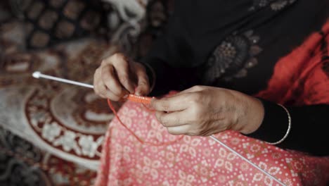 footage from above of woman siting and knitting with red wool and needle crafts