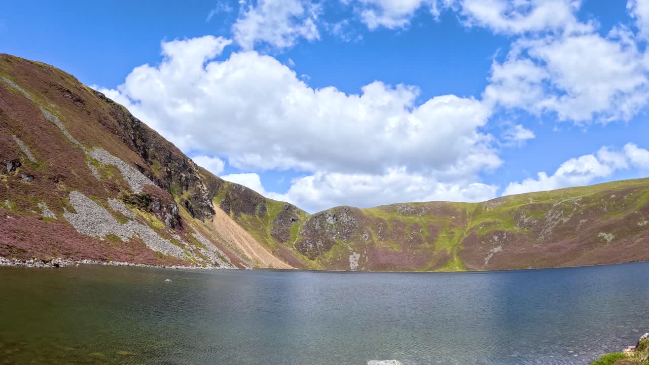 Clouds drift above Loch Brandy and surrounding hills in Glen Clova, Scotland. Wide static shot, natural daylight, vibrant colors, and dynamic sky movement