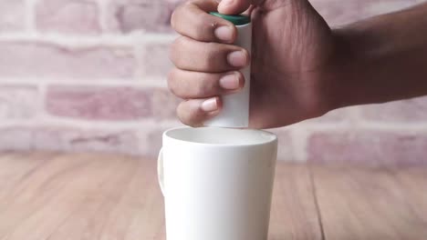 hand adding sugar or powder to a white mug