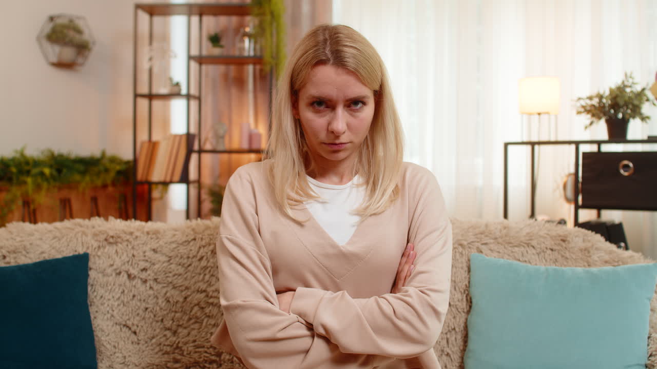 Adult woman spreading hands at home on sofa showing frustration and dissatisfaction after bad news
