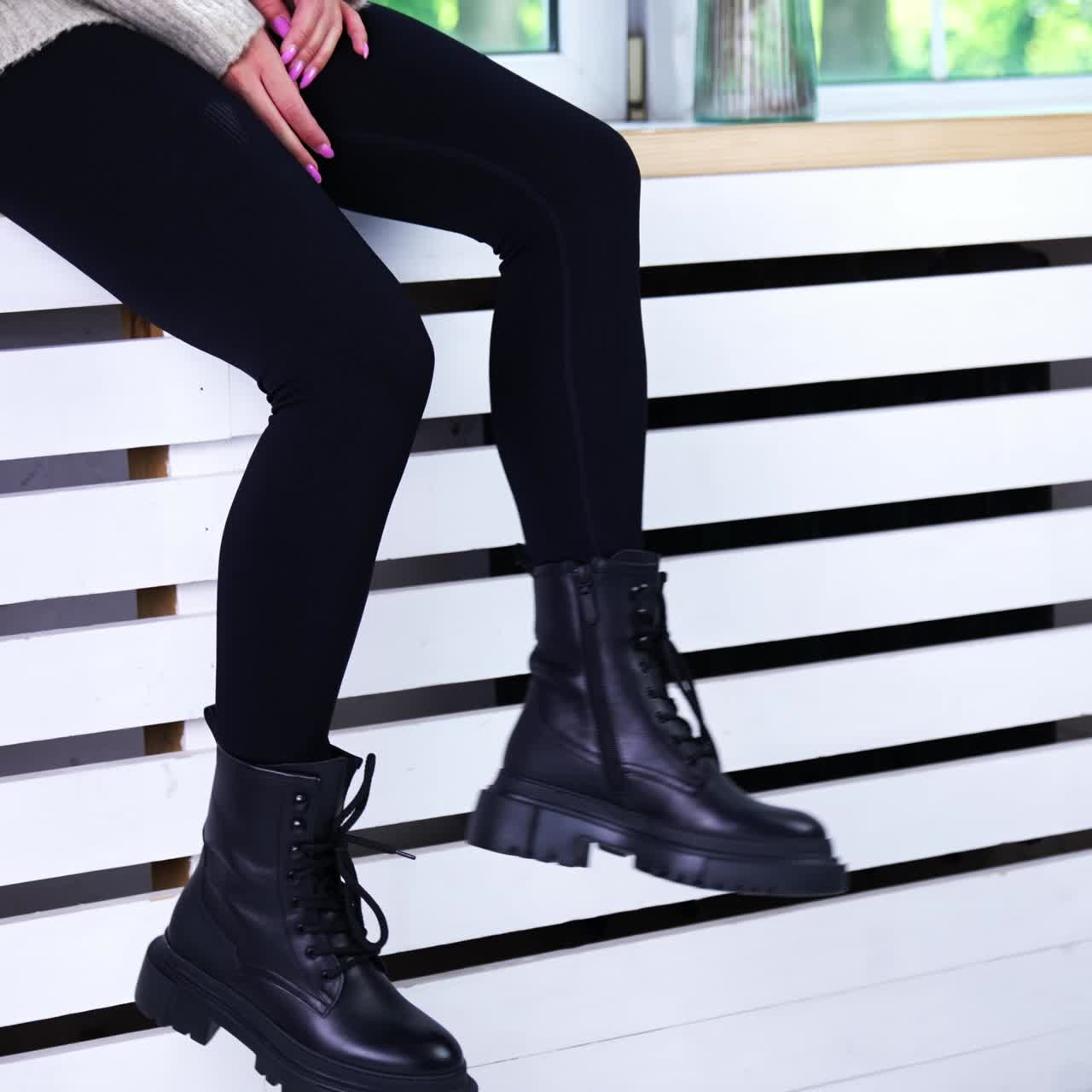 Female model sitting on the widow-sill demonstrating her footwear. Lady in black pants shows the black tractor boots with laces