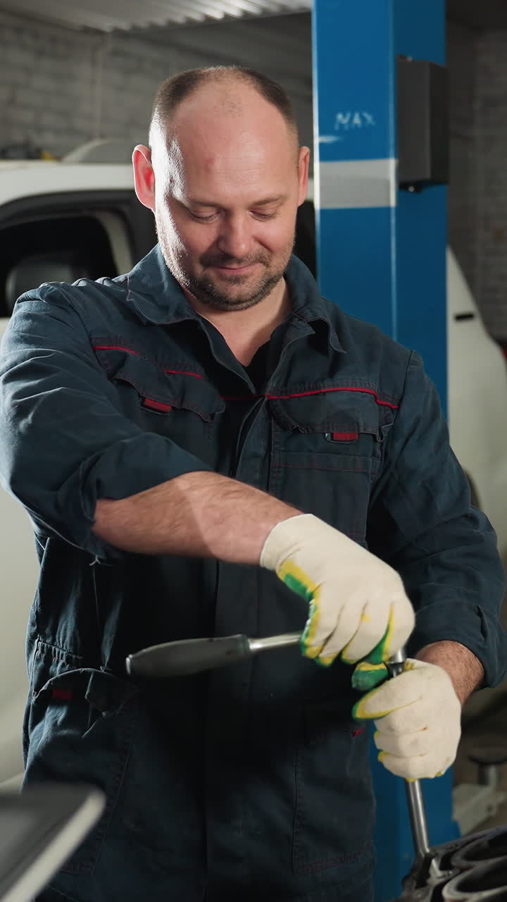 los estudiantes observan a un mecánico que demuestra el uso de llaves en el motor de un automóvil en un taller mecánico, el mecánico sonríe mientras maneja la herramienta, un espacio de trabajo industrial lleno de vehículos