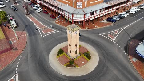 overhead drone footage captures cars and a semi-truck navigating a roundabout with a central clock tower in a small australian town under daylight