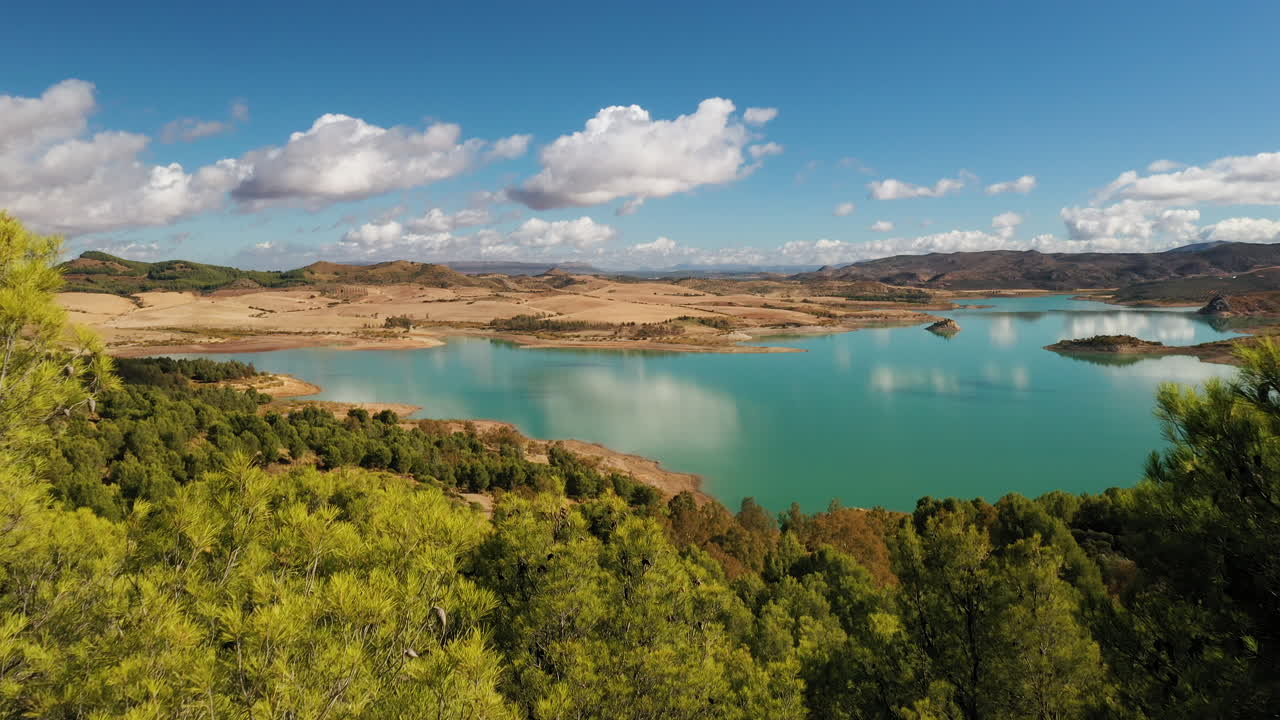 revelando toma aérea de drones de un lago de color cian rodeado por un desierto rocoso, paisajes y bosques.