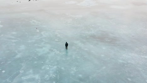 Aerial-shot-of-lonely-man-walking-on-ice-and-performing-a-dance-turn-on-a-vast-and-empty-frozen-lake-near-Reykjavík,-in-Iceland