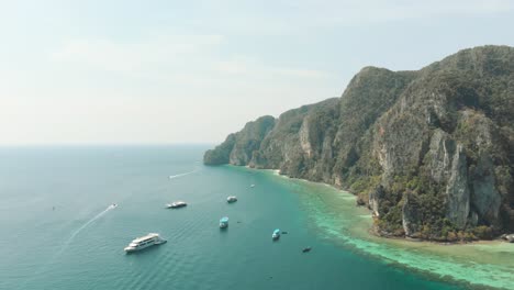 Costa-Idílica-Junto-Con-Aguas-Cálidas-Y-Exóticas-Obstaculizadas-Por-Un-Acantilado-Cerca-De-La-Cala-De-La-Playa-Pirata,-En-La-Isla-De-Ko-Phi-Phi-Don,-Tailandia---Toma-Aérea-Sobrevolada