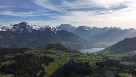 Der-Ruhige-Charme-Von-Amden-Und-Arvenbüel,-Schweiz,-Durch-Fesselnde-Drohnenaufnahmen,-Die-Grüne-Berge,-Ein-Charmantes-Dorf-Mit-Hohen-Bäumen-Und-Einen-Mit-Dünnen-Weißen-Wolken-Bedeckten-Himmel-Zeigen