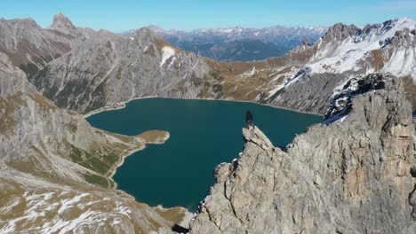 aerial shot of three friends sitting down on the edge of the mountain, relaxing and enjoying the fantastic view in front of them, overlooking lunersee and the love heart lake in the valley below