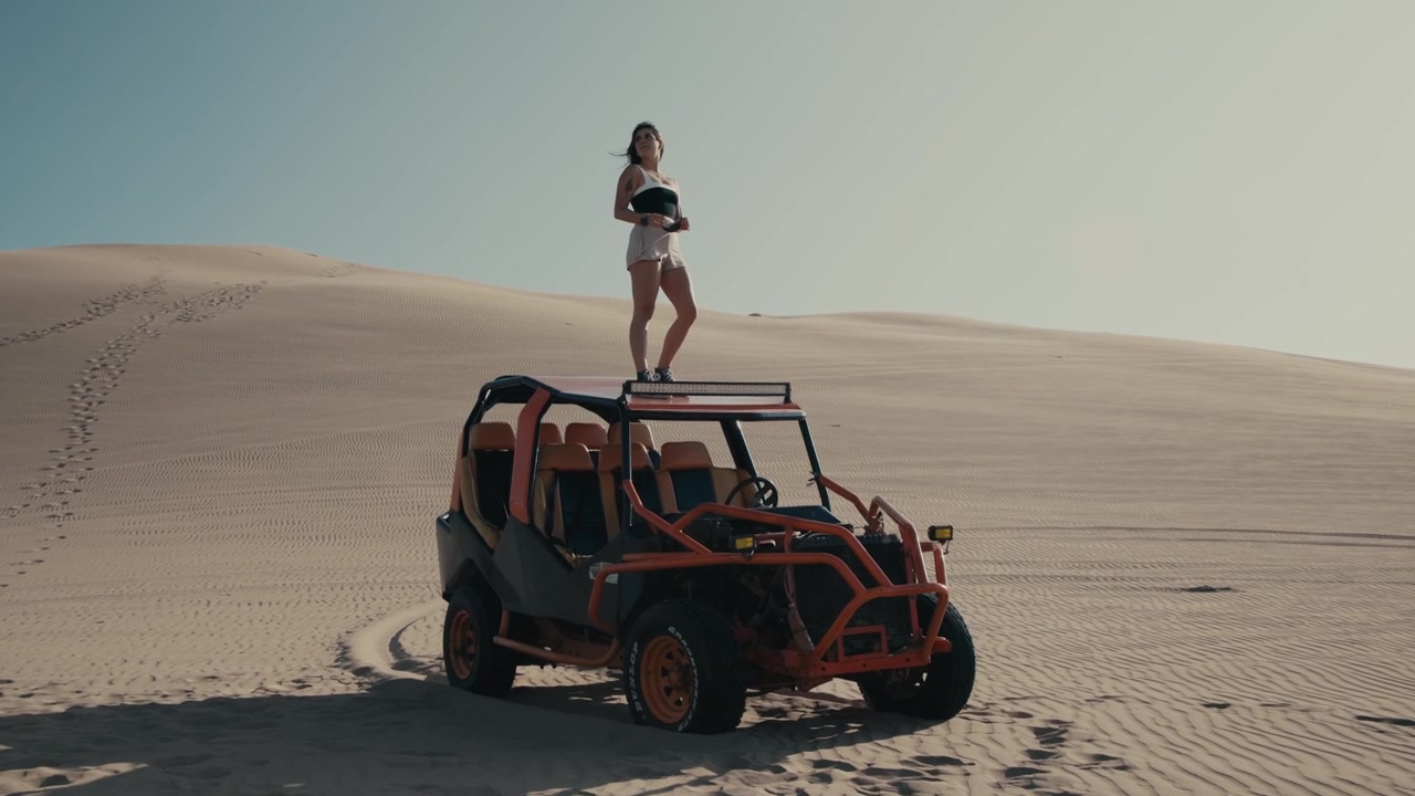 Wunderschöne Frau steht auf einem Dünenbuggy und posiert in der Wüste Perus vor der Kamera. Statische Aufnahme.