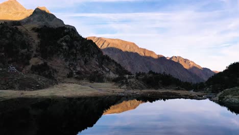 reflejando el tranquilo lago lac d&#39;espingo en haute-garonne, montañas de los pirineos, francia con el sol golpeando los picos, toma aérea baja