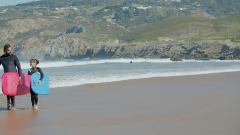 surfer with artificial leg and daughter holding surfboard and talking while walking on the beach