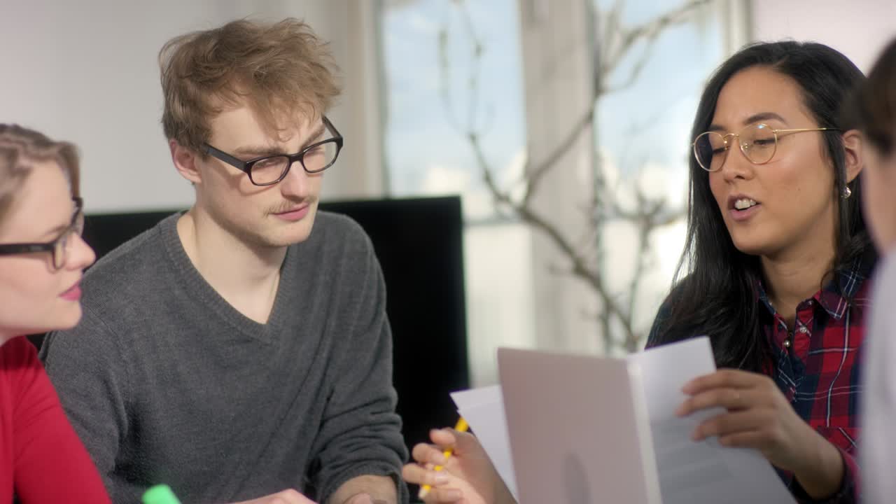 joven mujer de negocios asiática explicando sábanas a sus compañeros de trabajo con gafas en la mesa