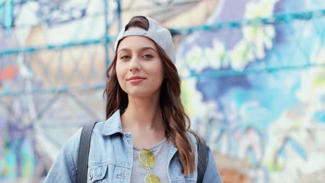 caucasian woman in hipster style wearing cap and looking at the camera in the street