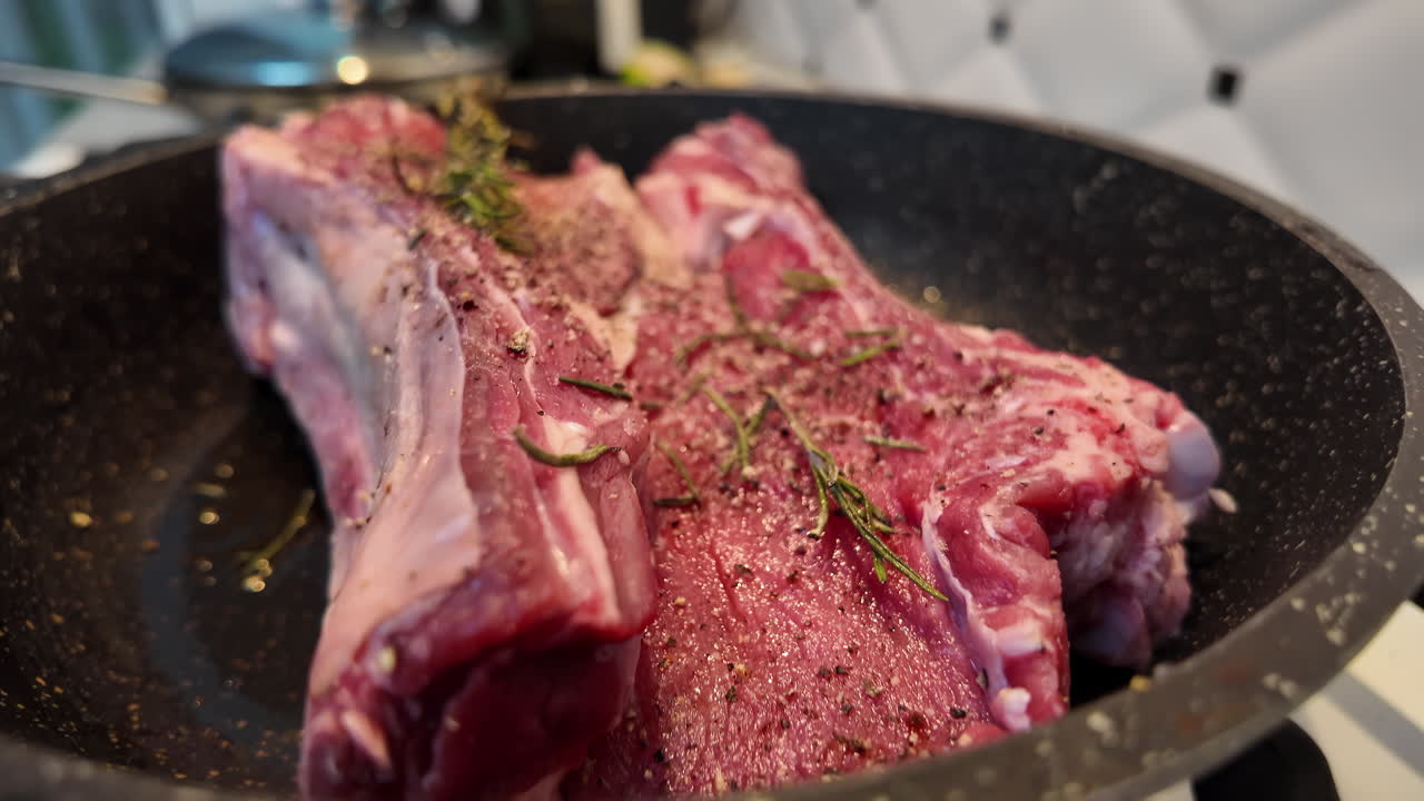 Big red beef stake on a black pan with rosemary ready for cooking, black pepper on top