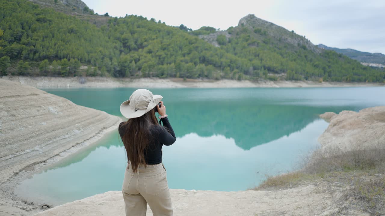 Woman photographing a turquoise lake in a mountainous area
